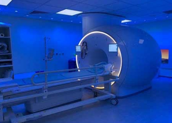 A modern MRI machine in a room with blue ambient lighting, accompanied by a patient bed on a movable platform.